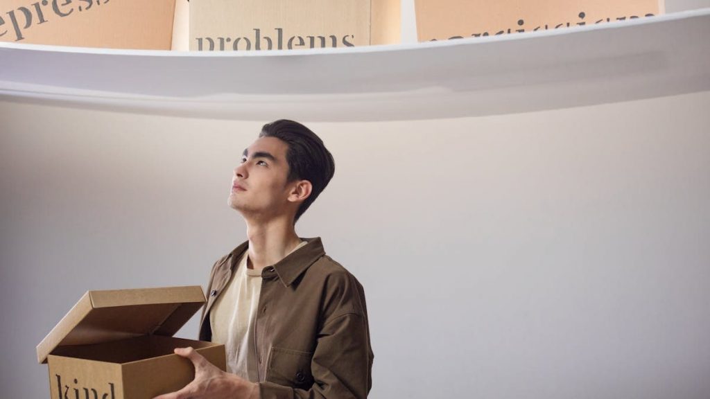 A thoughtful man indoors holding a box labeled 'kind', surrounded by words like 'problems'.