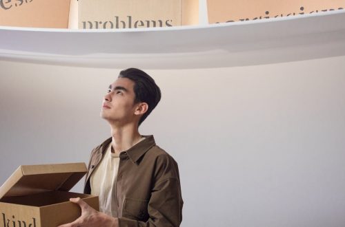 A thoughtful man indoors holding a box labeled 'kind', surrounded by words like 'problems'.